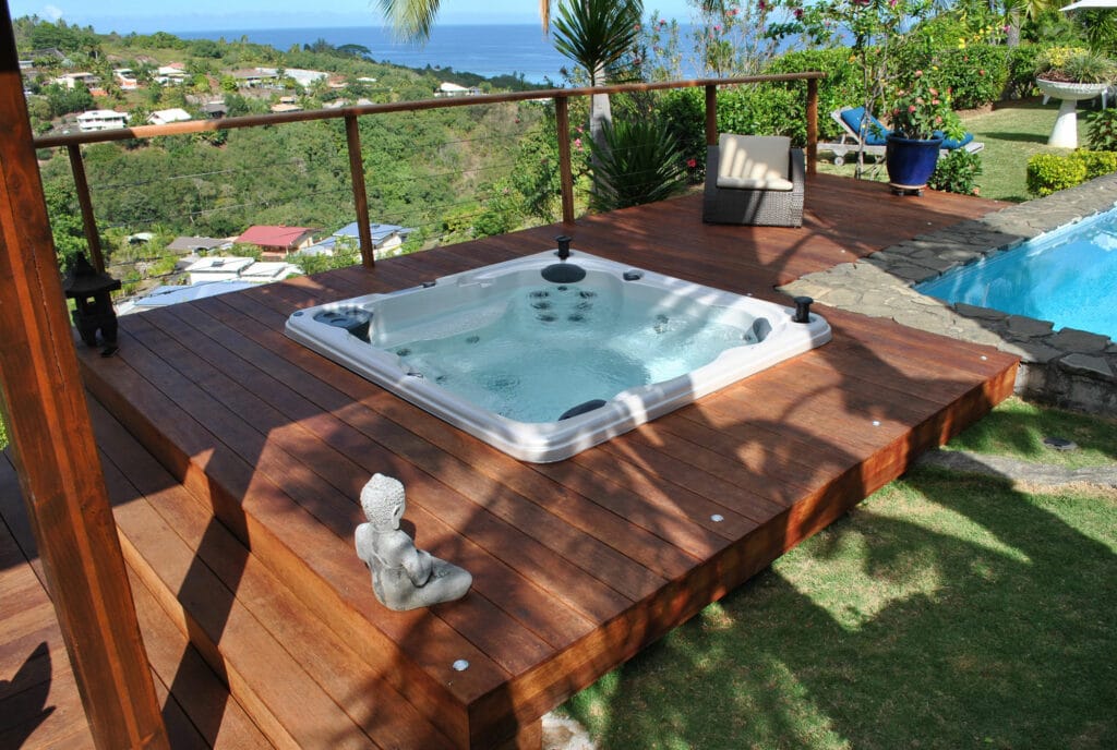 Swim spa with a blue interior and multiple jets, sitting outdoors surrounded by wooden decking and greenery